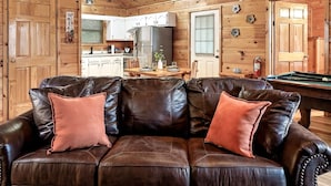A cozy wooden interior with a leather sofa, a pool table, and a kitchen area. - Views I Firepit I Pool Table I Hot Tub I Sleeps 4 (Sevierville)