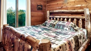 A wooden cabin bedroom with a large bed, a ceiling fan, and a window with curtains. - Views I Firepit I Pool Table I Hot Tub I Sleeps 4 (Sevierville)