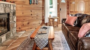 A cozy cabin interior with a stone fireplace, wooden walls, a leather sofa, and a bench. - Views I Firepit I Pool Table I Hot Tub I Sleeps 4 (Sevierville)