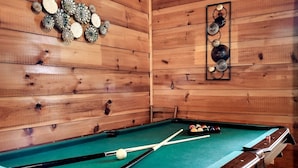 A pool table in a wooden room with a green felt surface, surrounded by wooden walls and a ceiling.