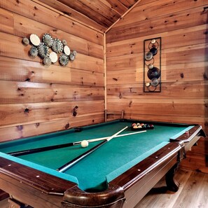 A pool table in a wooden room with a green felt surface, surrounded by wooden walls and a ceiling. - Views I Firepit I Pool Table I Hot Tub I Sleeps 4 (Sevierville)