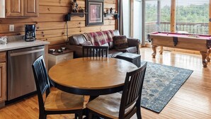 Un intérieur de chalet chaleureux avec un plafond en bois, un coin repas avec une table ronde et des chaises, un canapé, une machine à café et une table de billard.