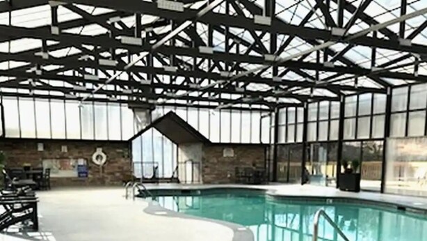 Un espace piscine intérieur offrant une vue dégagée sur le bassin, un coin salon avec des chaises et une plante en pot posée sur une table.