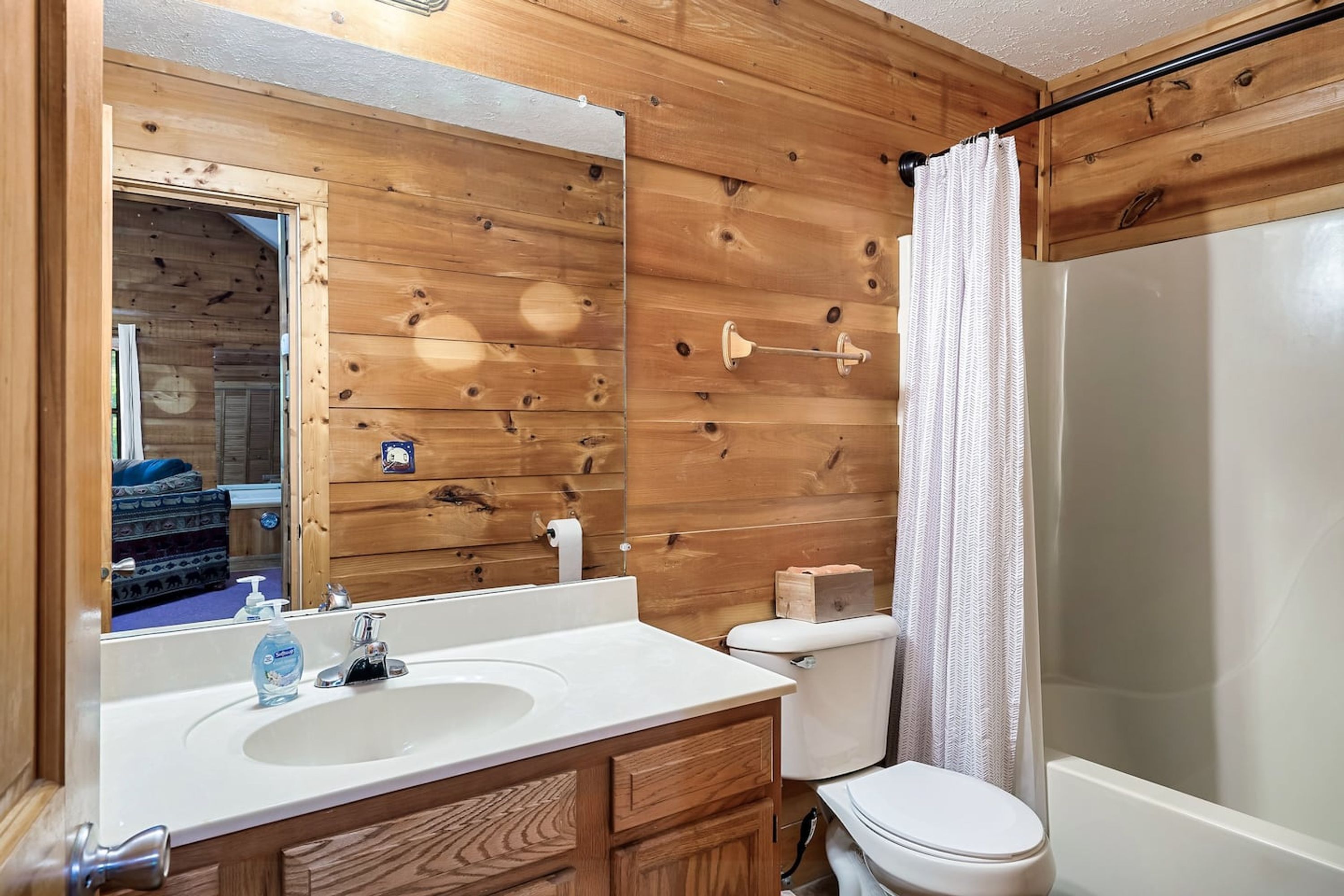 A wooden-paneled bathroom with a sink, toilet, and shower.
