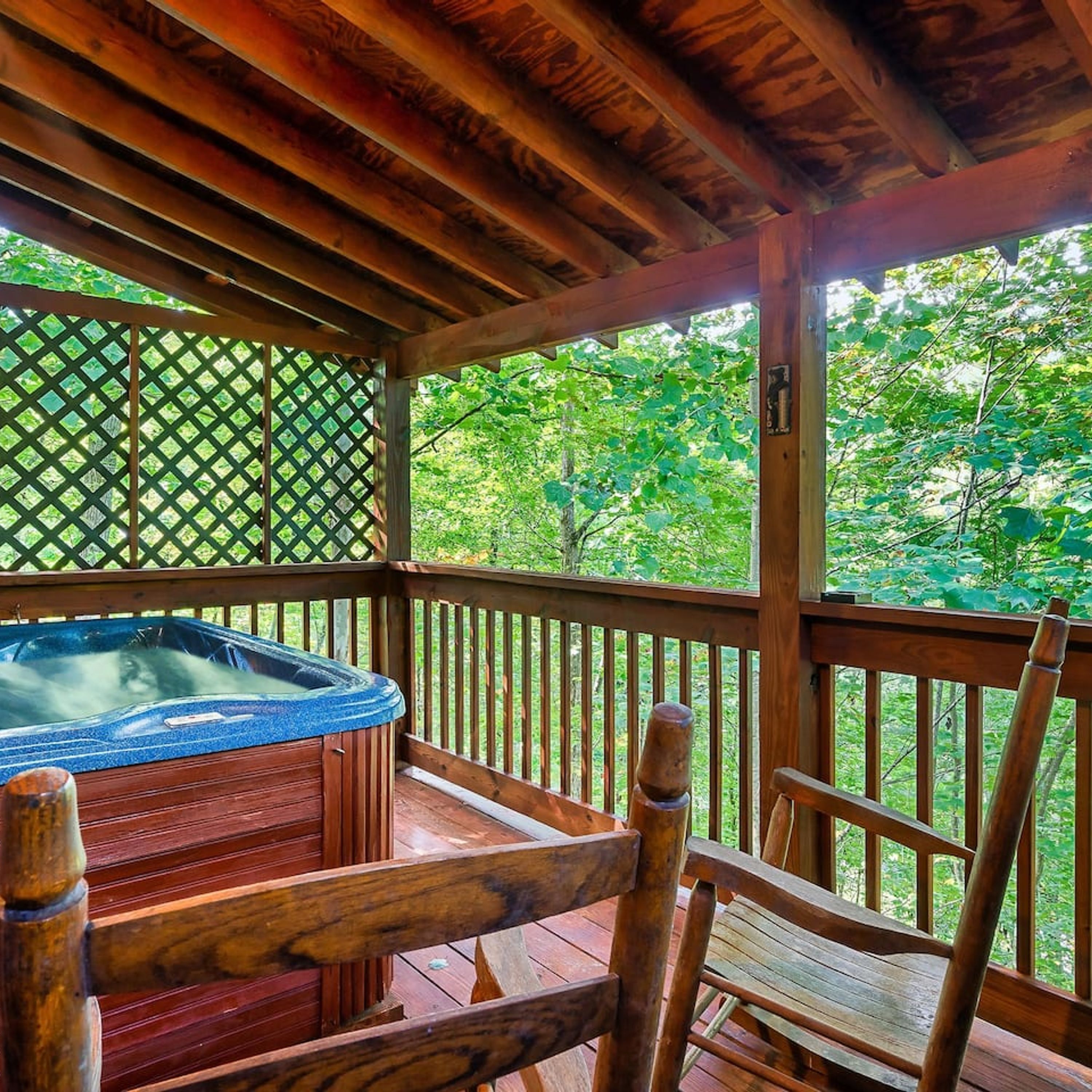 A wooden deck with a hot tub, wooden chairs, and a lattice fence.