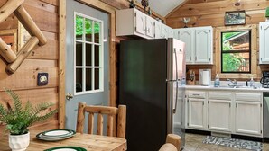 Un interior de madera con una mesa de comedor, sillas, un refrigerador y armarios blancos.