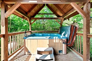 Relax in a hot tub on a deck surrounded by lush greenery.