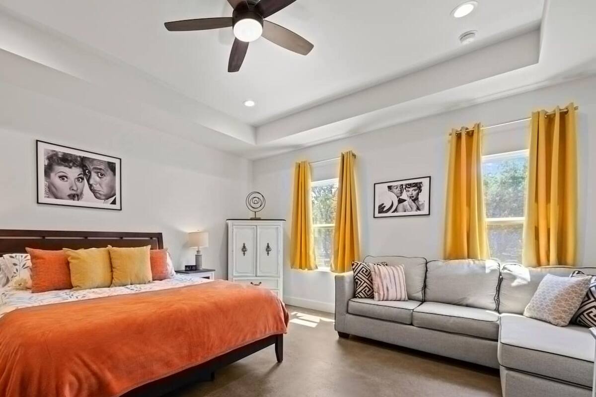 A bedroom with a bed, a sofa, a cabinet, and two windows with curtains.