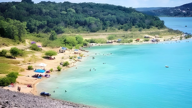 Una playa con agua turquesa cristalina, una orilla arenosa y una colina boscosa al fondo.