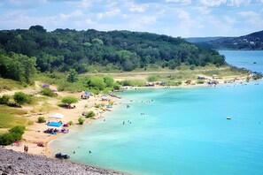 A beach with clear turquoise water, a sandy shore, and a forested hill in the background. - Family/event Retreat Sleeps 28 Amenities Galore (Wimberley)