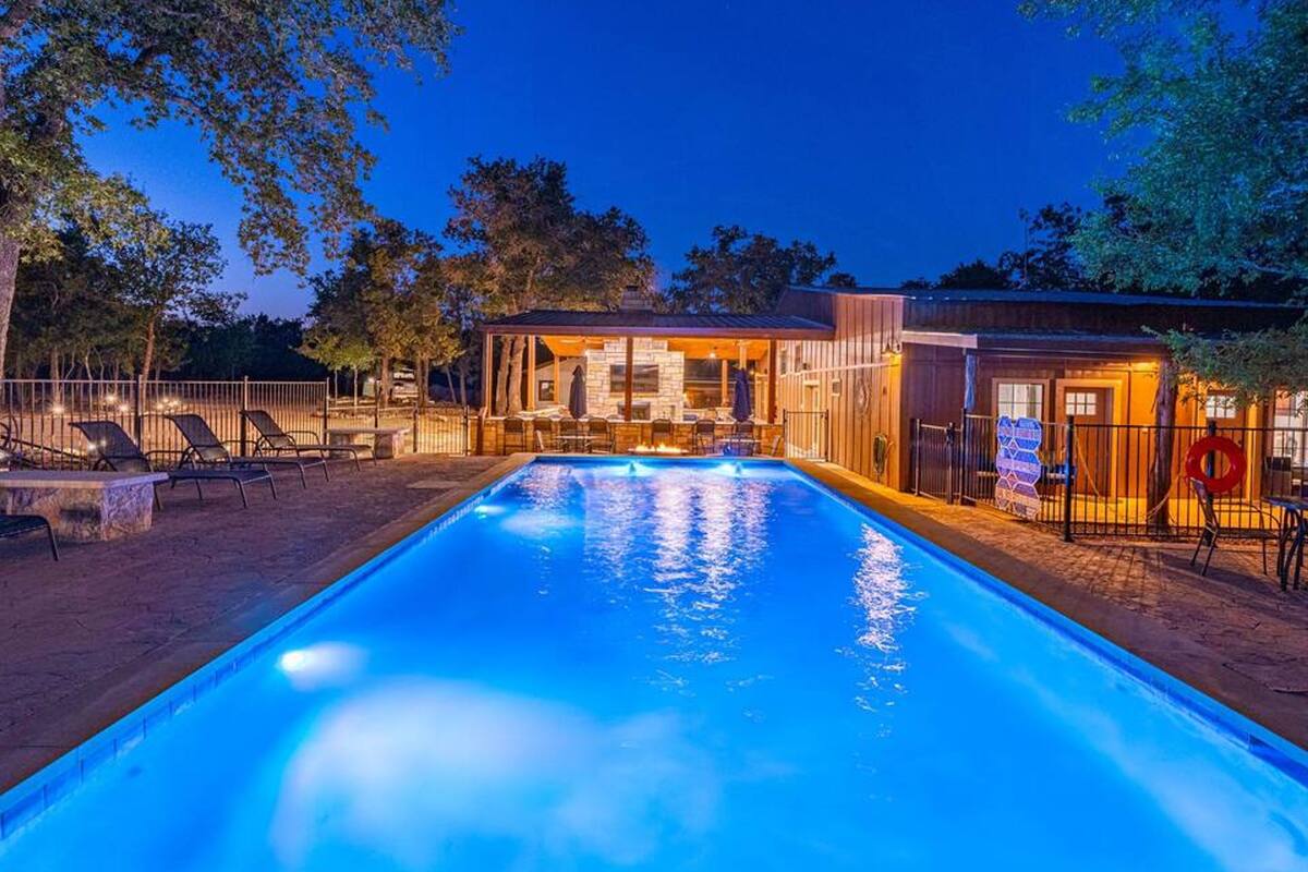 A swimming pool with a clear blue water surface, surrounded by lounge chairs and a covered seating area.