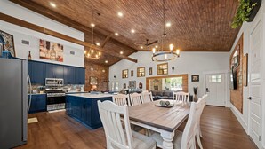 Una cocina amplia con armarios de madera, una isla central y un comedor con una gran mesa de madera y sillas blancas.
