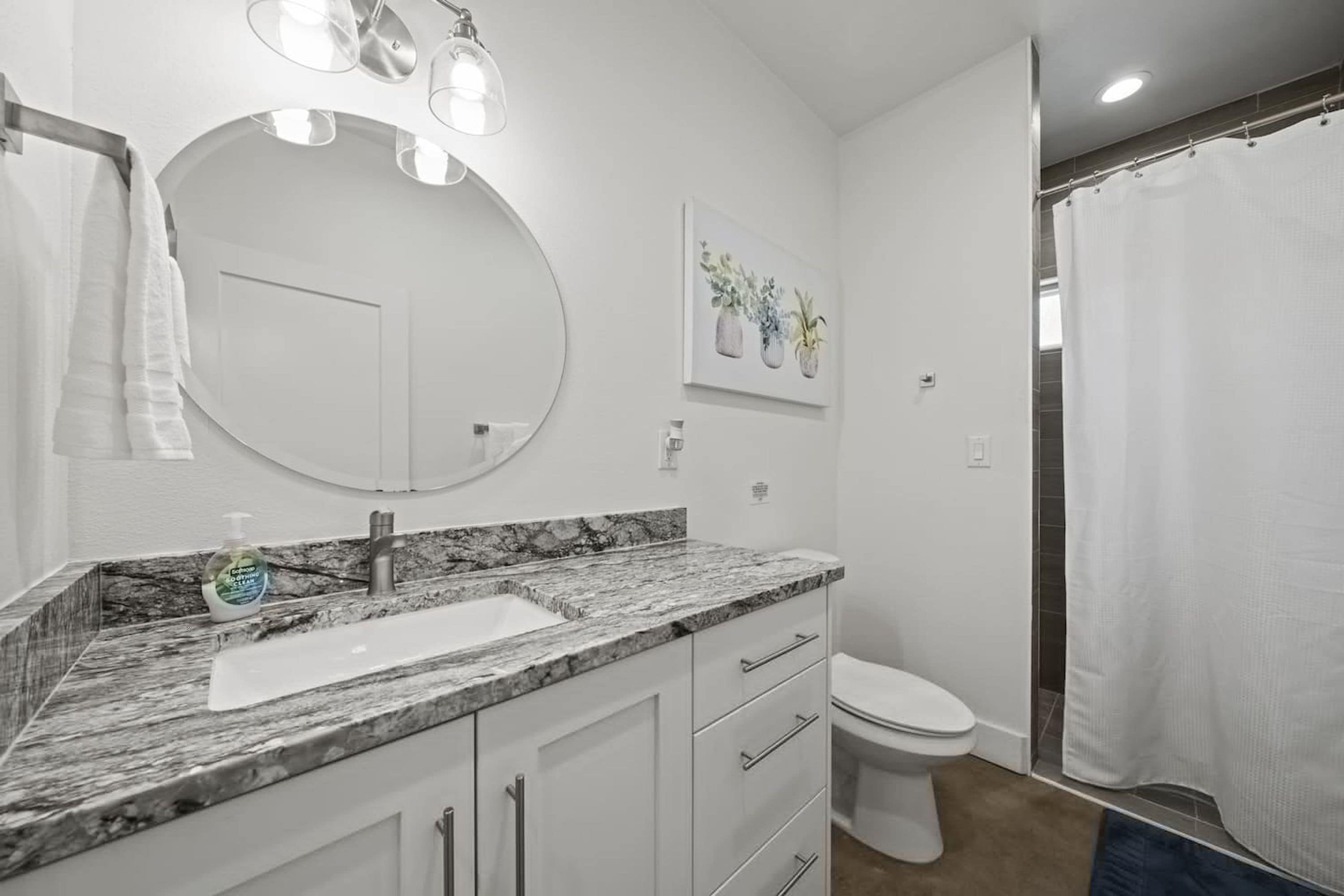 Une salle de bain avec un lavabo en marbre, un grand miroir, des toilettes et un rideau de douche.