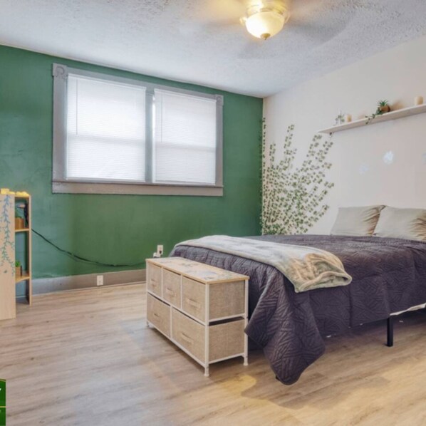 Une chambre à coucher avec un lit, une commode, une fenêtre et un mur orné d’une plante.