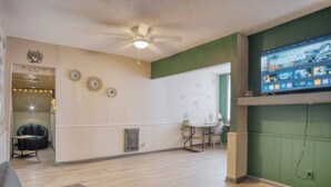 A living room with a ceiling fan, a television displaying 'Mandalorian', a dining area with a table and chairs, and a green accent wall. - Artistic 1BR - APT - Near Downtown Mass Ave (Indianapolis)