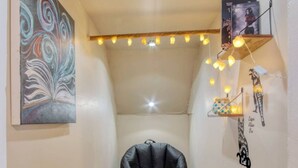 A narrow hallway with a black bean bag chair, a small wooden table, and string lights on the ceiling. - Artistic 1BR - APT - Near Downtown Mass Ave (Indianapolis)
