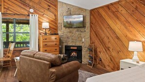 Una habitación acogedora con chimenea de piedra, paredes de madera, un sofá cómodo y una cama.
