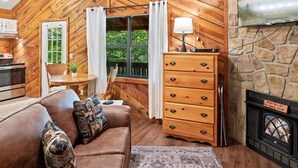 Interior acogedor de una cabaña con paredes de madera, una chimenea, un sofá, una mesa de comedor y un televisor montado en una pared de piedra.