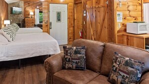 Interior acogedor de una cabaña con techo de madera, una cama, un sofá y una chimenea de piedra.