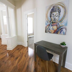 Quarto com piso de madeira, uma mesa com cadeira, pintura de Buda na parede e um vaso com planta.