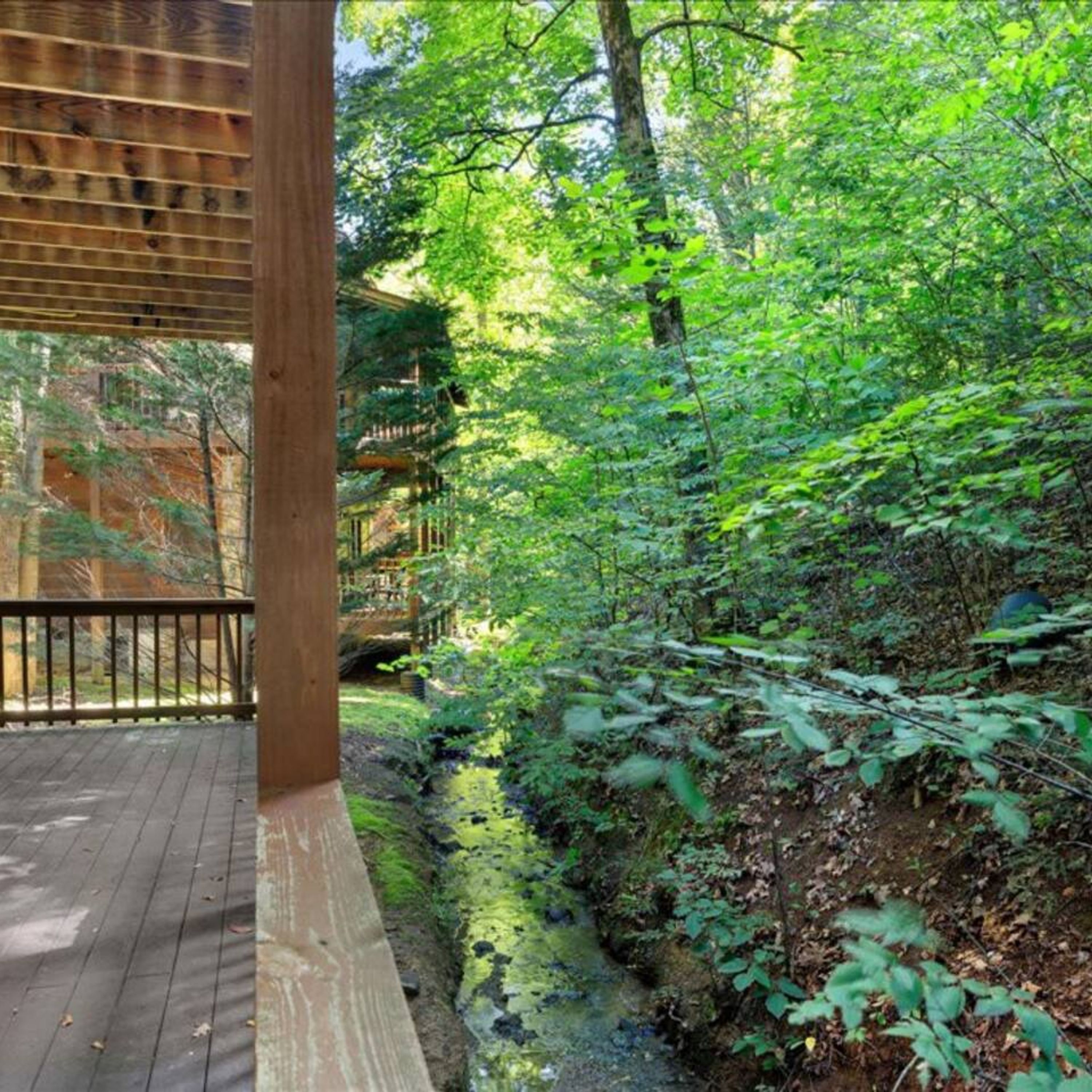A wooden deck with a view of a forested area and a small stream.