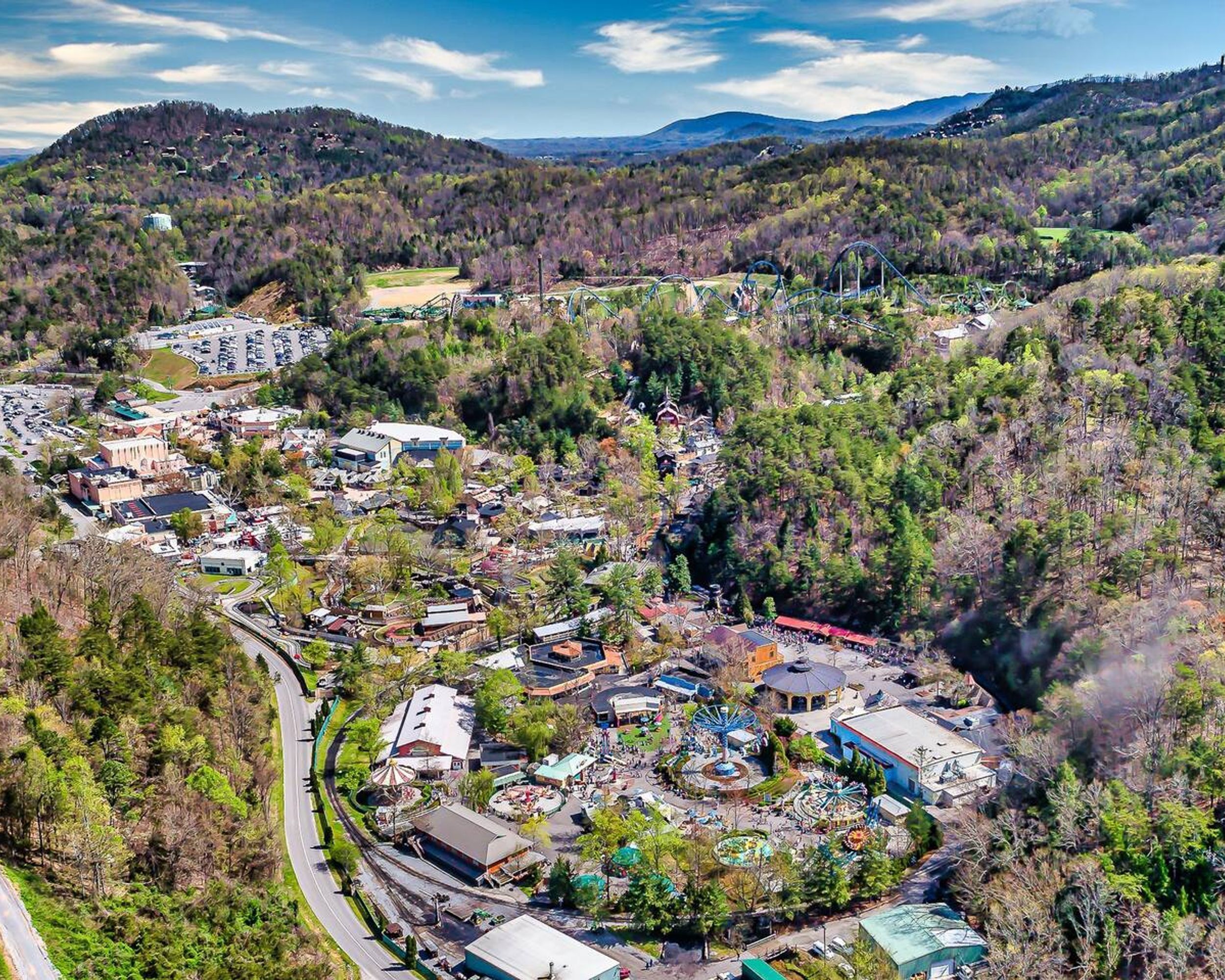 An aerial view of a town with a mix of residential and commercial buildings, surrounded by forested hills.