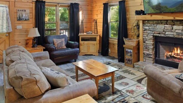 A cabin interior with a fireplace, wooden walls, a sofa, and a television.