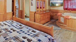A wooden cabin interior with a bed, dresser, vanity, and a ceiling fan.