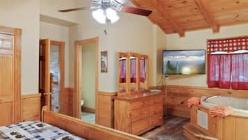A wooden cabin interior with a bed, dresser, vanity, and a ceiling fan.