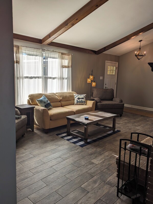 A living room with a beige sofa, a wooden coffee table, and a chair. There is a window with sheer curtains, a lamp, and a door in the background. - 180 Degree Seneca Lake Views, privacy galore with hot tub. Sleeps 9
(Senecaville)