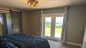 A bedroom with a bed, a ceiling light, a sliding door to a balcony, and a view of greenery. - 180 Degree Seneca Lake Views, privacy galore with hot tub. Sleeps 9
 (Senecaville)