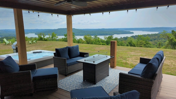 A covered outdoor seating area with wicker furniture, a hot tub, and a view of a lake and mountains. - 180 Degree Seneca Lake Views, privacy galore with hot tub. Sleeps 9
 (Senecaville)
