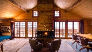A cozy log cabin interior with a fireplace, wooden walls, and large windows. - New in Grindelwald-Chalet Caramelle, Top of Grindelwald (Grindelwald)