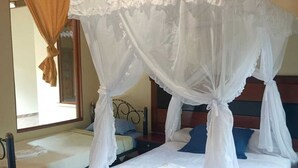 Une chambre avec un lit sous un baldaquin blanc, une fenêtre avec des rideaux et un lit doté d’une tête de lit.