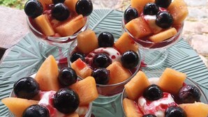 Un dessert servi dans un verre, composé de fruits et d’une garniture crémeuse, présenté sur une assiette verte.