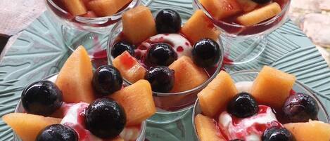 Postre en vaso con fruta y cobertura cremosa, sobre un plato verde.