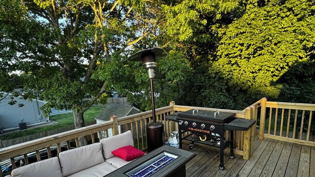A deck with a black grill, a white sofa with red cushions, and a table with a blue glass top.