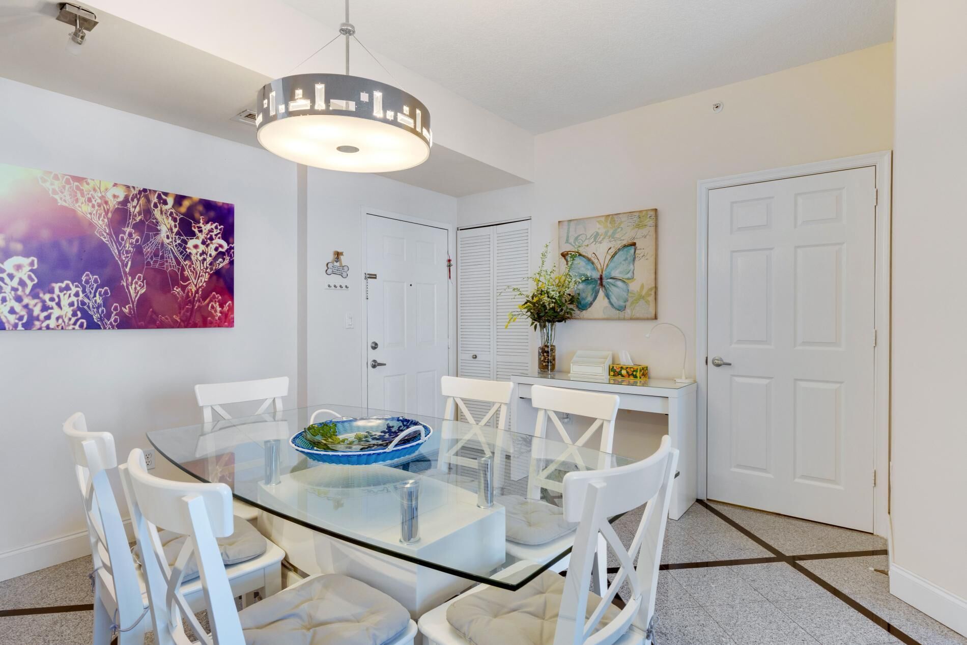 A modern dining area with a glass table, white chairs, and a decorative ceiling light.