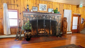 A room with a stone fireplace, wooden walls, a wooden floor, a wooden statue, and a door with an EXIT sign. - Camp Richardson Historic Resort (South Lake Tahoe)