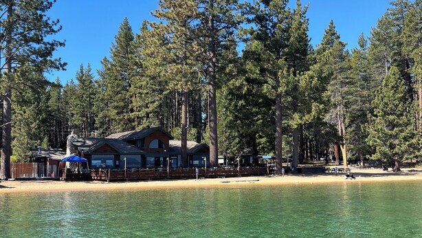 A lakeside cabin with clear water, surrounded by tall pine trees and a sandy beach. - Camp Richardson Historic Resort (South Lake Tahoe)