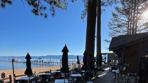 An outdoor seating area with tables and chairs, overlooking a beach and the ocean. - Camp Richardson Historic Resort (South Lake Tahoe)