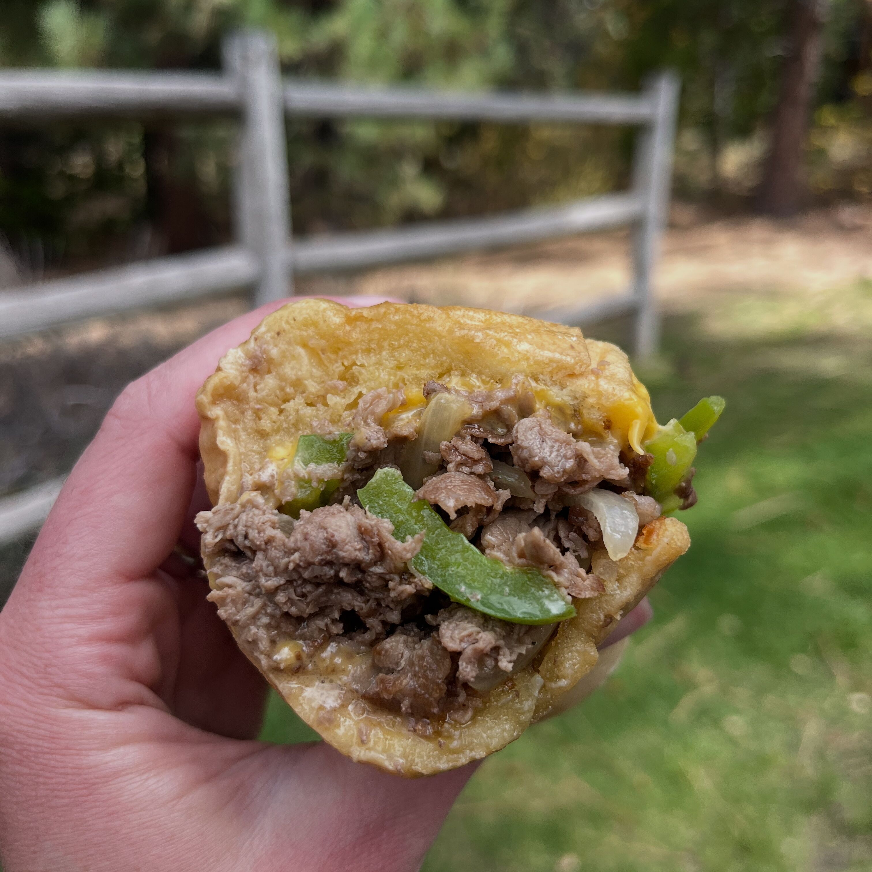 A hand holding a sandwich with visible ingredients like meat, corn, and green peppers.