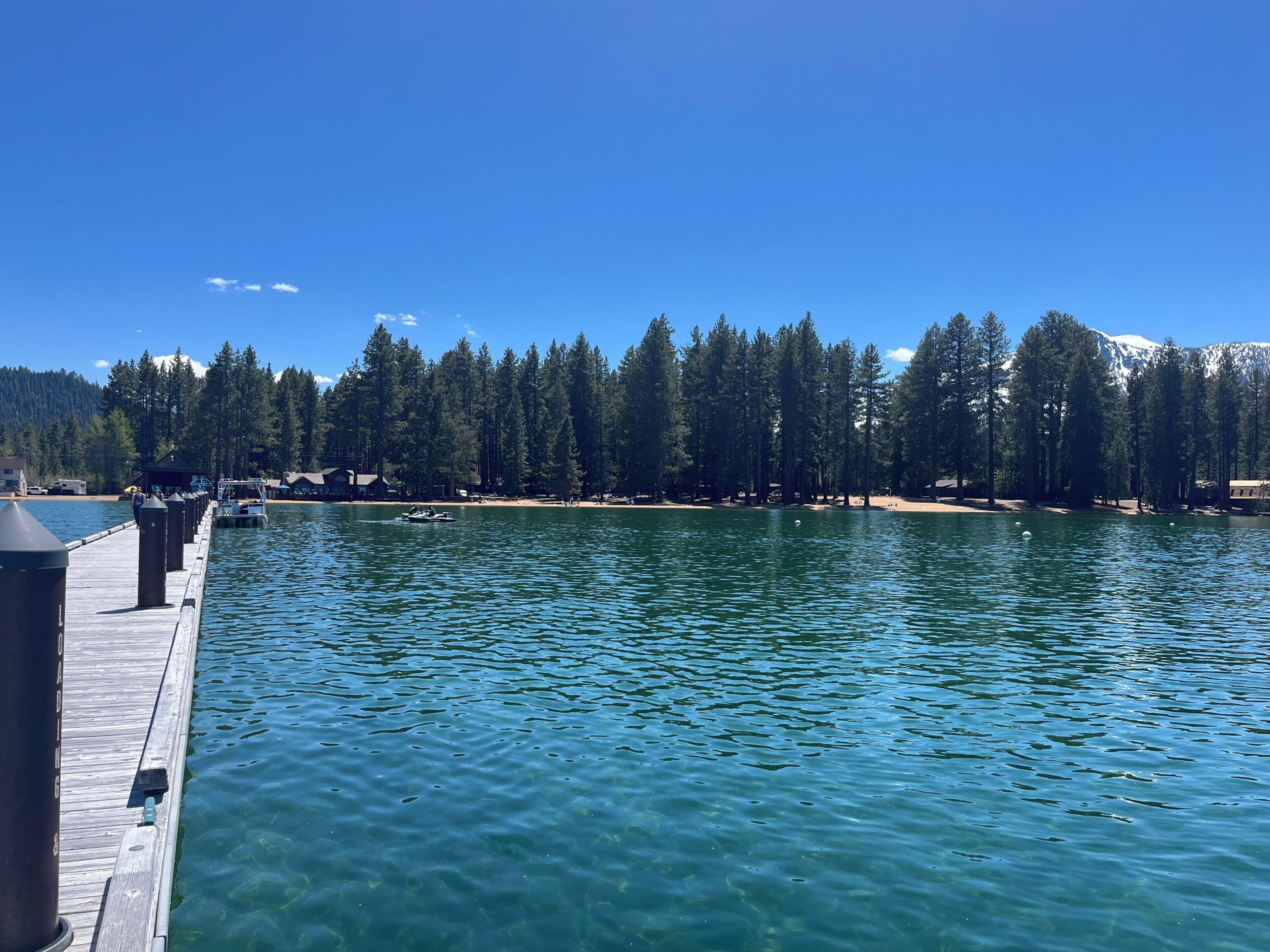 A dock extending into a calm lake with a forested shoreline and a mountain in the background.