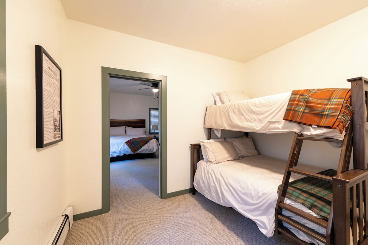 Ein Schlafsaalzimmer mit Etagenbetten, einem gerahmten Bild an der Wand und einer Tür zu einem weiteren Raum.