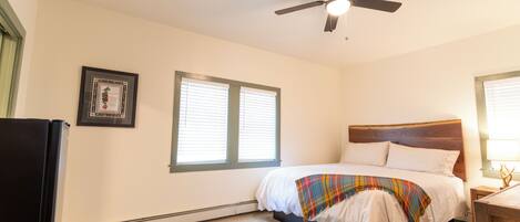 Ein Schlafzimmer mit einem Bett, einem Deckenventilator, einem Fenster und einem gerahmten Bild an der Wand.