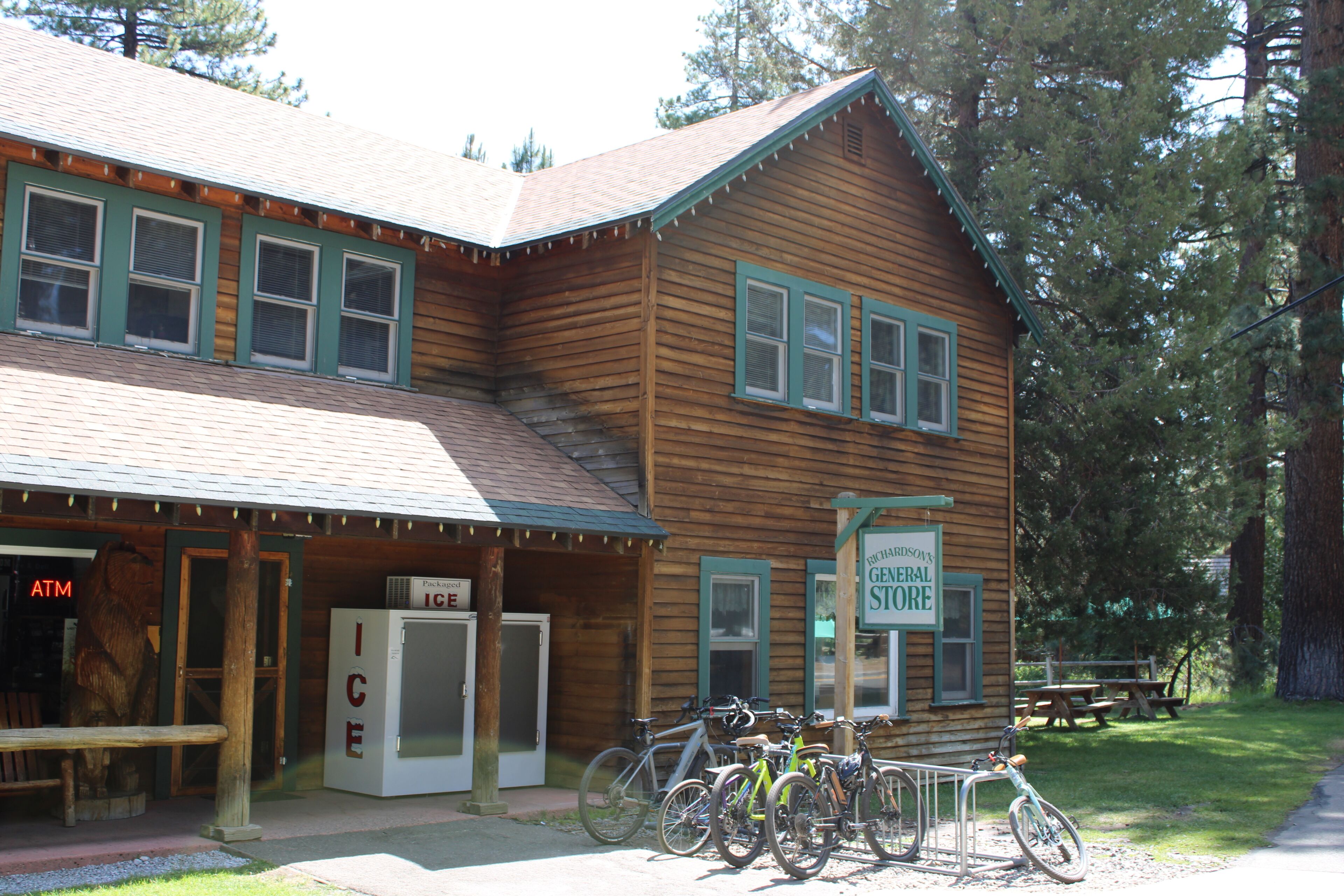 A wooden building with a sign for a general store, a refrigerator, and bicycles parked outside.