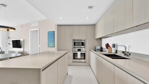 A modern kitchen with light wood cabinets, a built-in oven, and a stainless steel sink.
