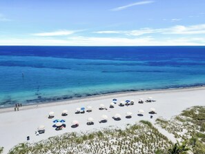 A beach with white sand, clear blue water, and beach umbrellas.