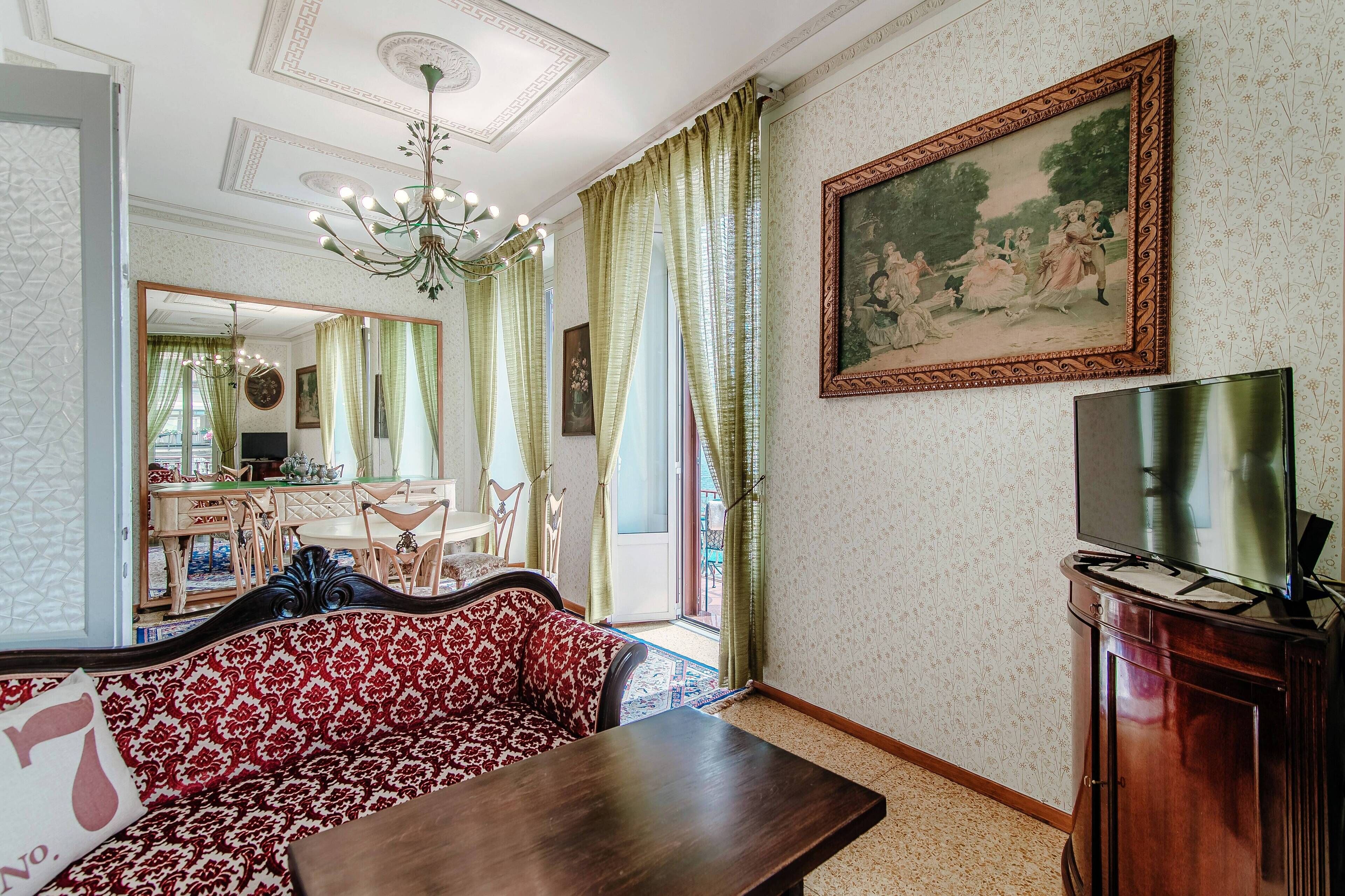 A living room with a sofa, a dining table, a TV, and a chandelier.