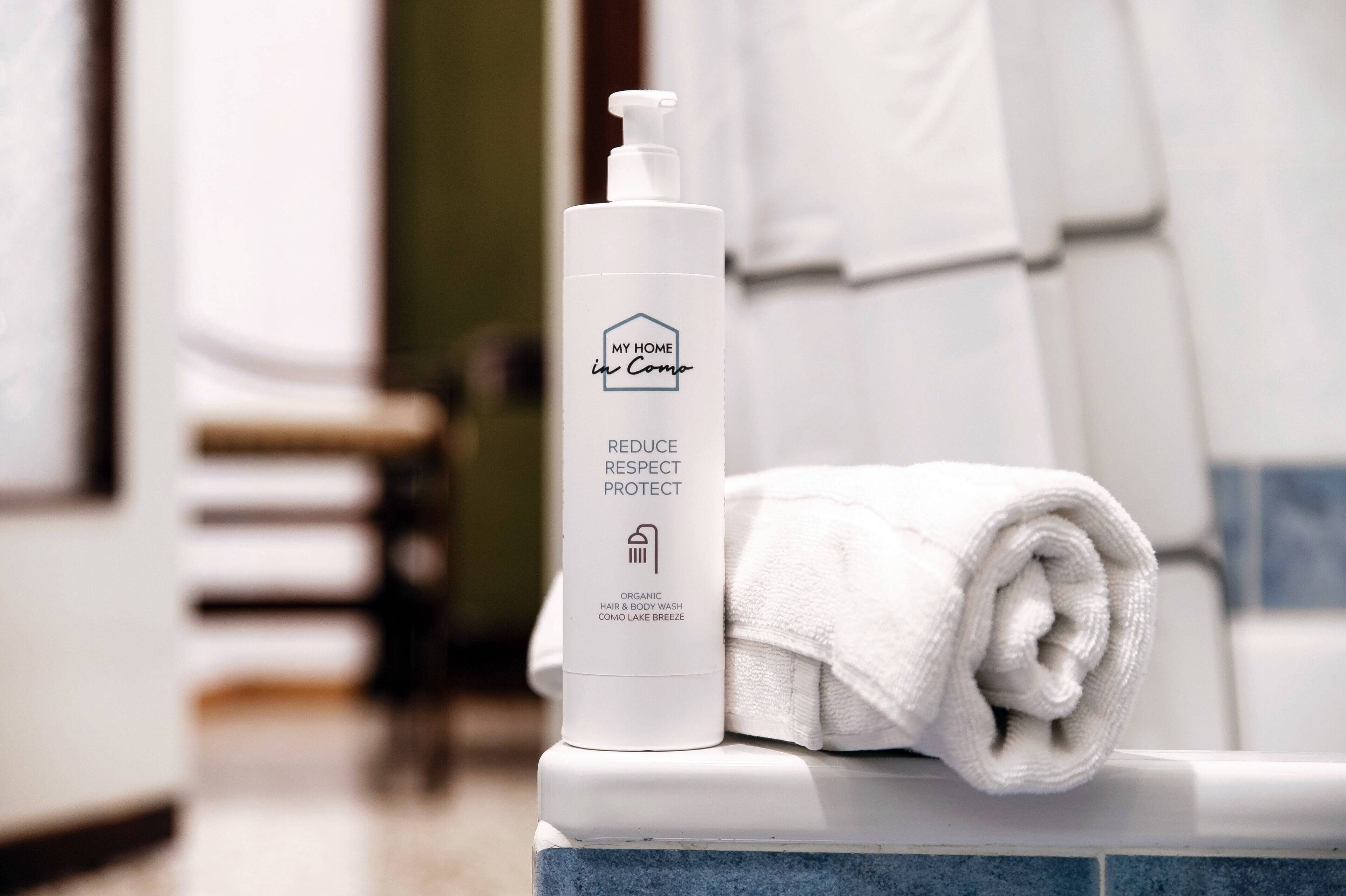 A bathroom with a white bottle labeled "MY HOME in Como" and a rolled white towel on a counter.